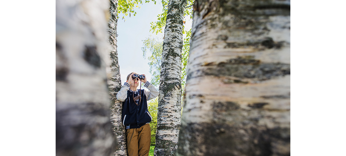 ein Mädchen steht neben einer Birke und schaut durch ihr Fernglas