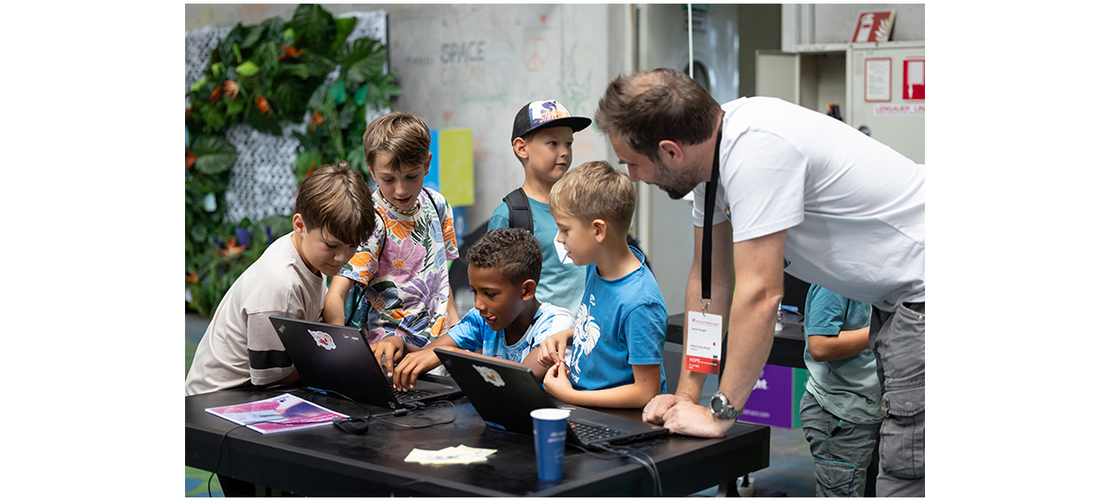 Lehrerin mit einer Gruppe von Kindern um einen Laptop herum