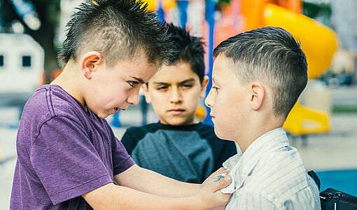 Ein junger Schüler drangsaliert einen anderen Schüler und ein dritter Schüler schaut zu