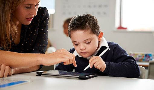 Lehrerin zeigt einem beeinträchtigtem Schüler etwas auf dem Tablet