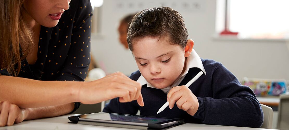 Lehrerin zeigt einem beeinträchtigtem Schüler etwas auf dem Tablet